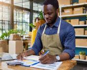 Firefly small business owner looking busy while working on paperwork at a desk with shop in the back → Green Country Federal Credit Union Small business owners will need to file Beneficial Ownership Reports starting January 1 2024