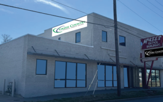 Exterior view of a brick commercial building with large storefront windows and a street sign reading Green County against a blue sky